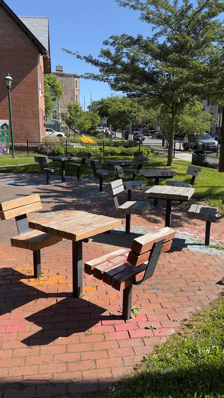 A cluster of small chess-style tables on a brick plaza at the front of Audrey Carey Park.