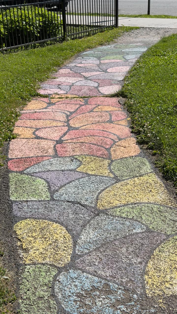 A faded chalk-painted rainbow stone-mosaic path running between green grass at Audrey Carey Park.