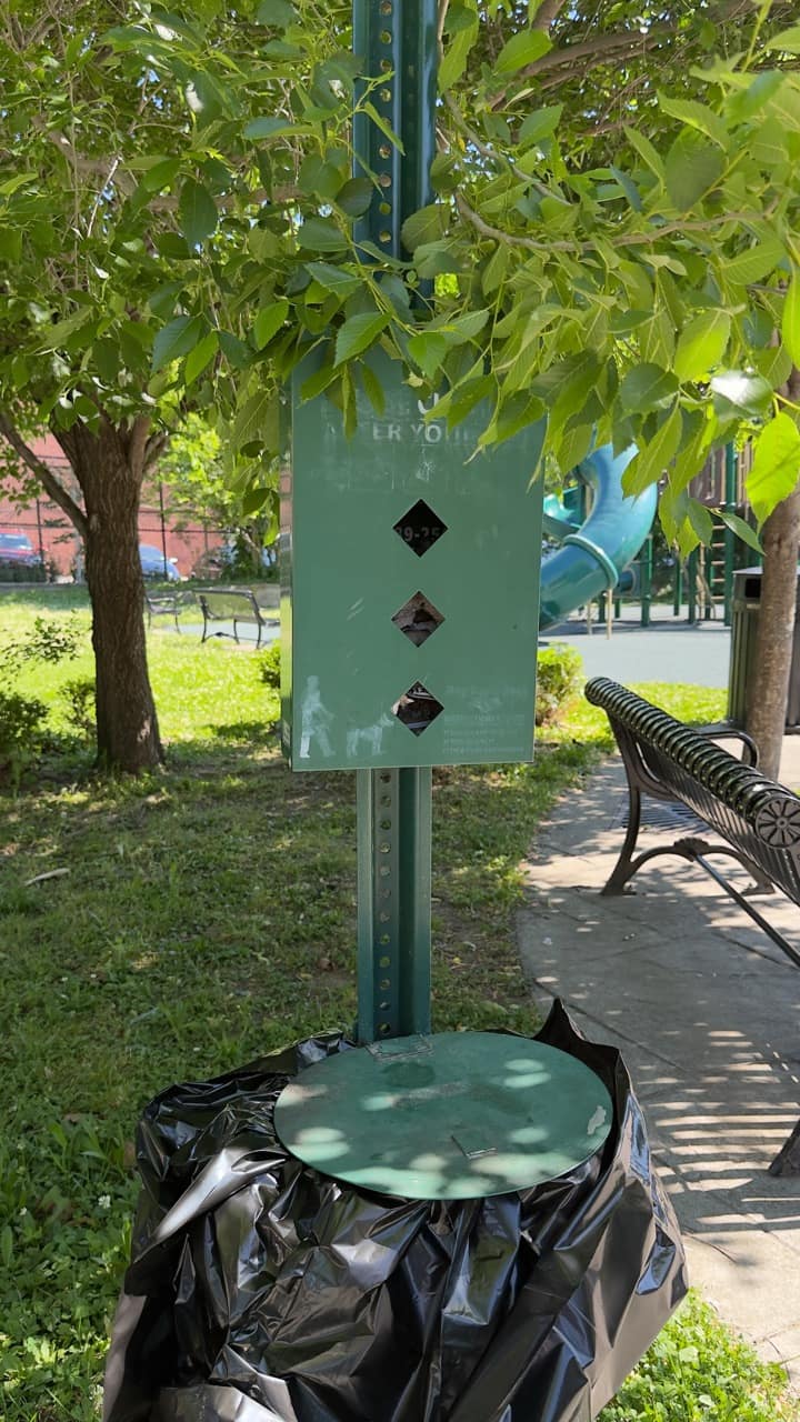 A green metal dog waste station next to a paved path at Tyrone Crabb Park.