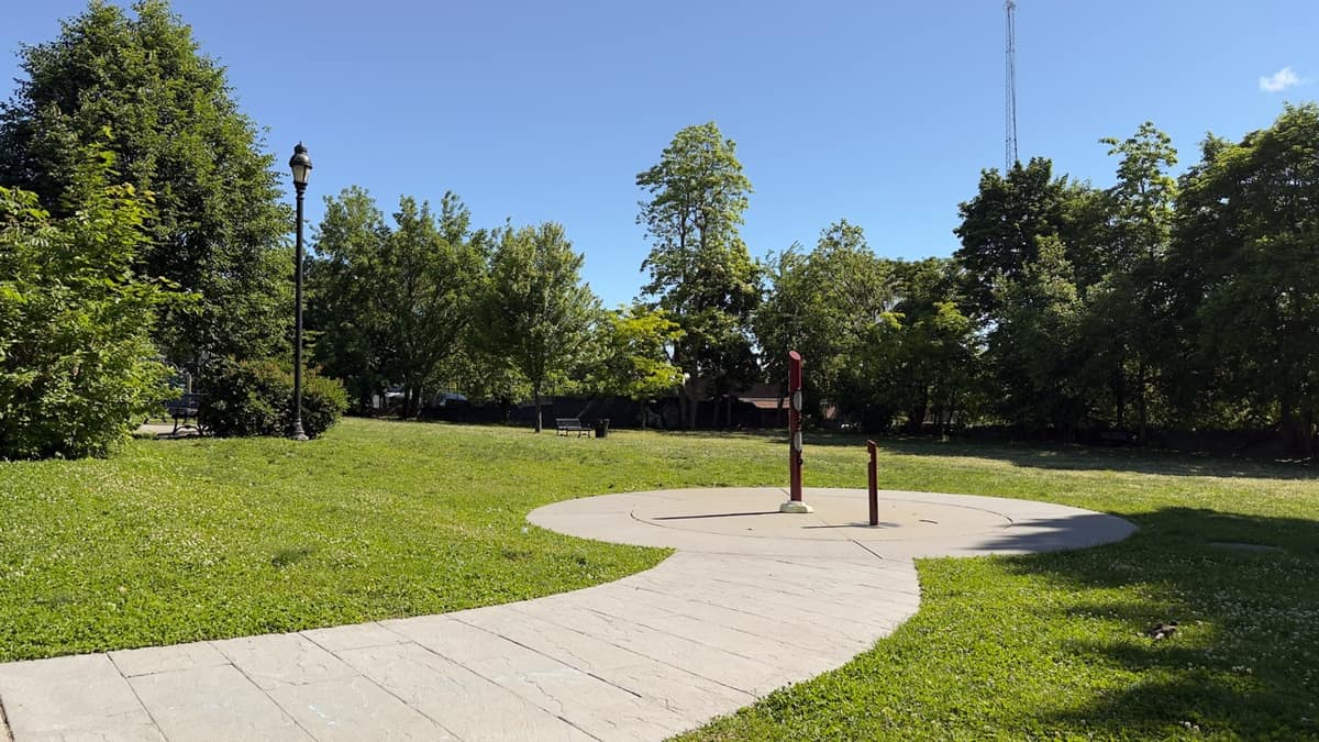 The blue splash pad at Tyrone Crabb Park, ringed by an iron fence with a brick church behind.