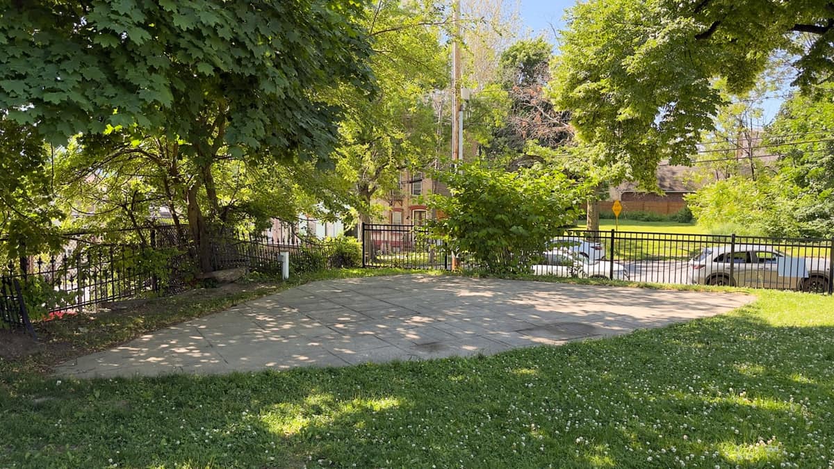 A small concrete pad inside Tyrone Crabb Park ringed by trees and an iron fence.
