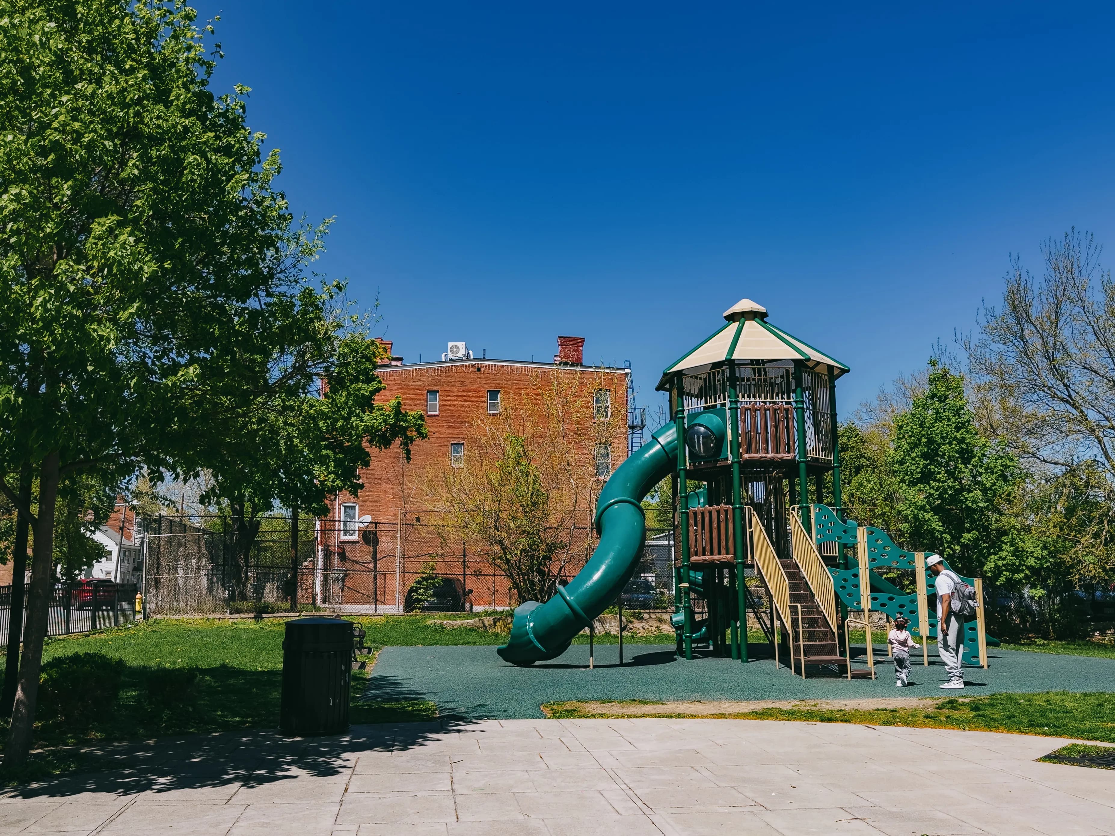 A green twisting slide tower at Tyrone Crabb Park, with a child playing alongside.