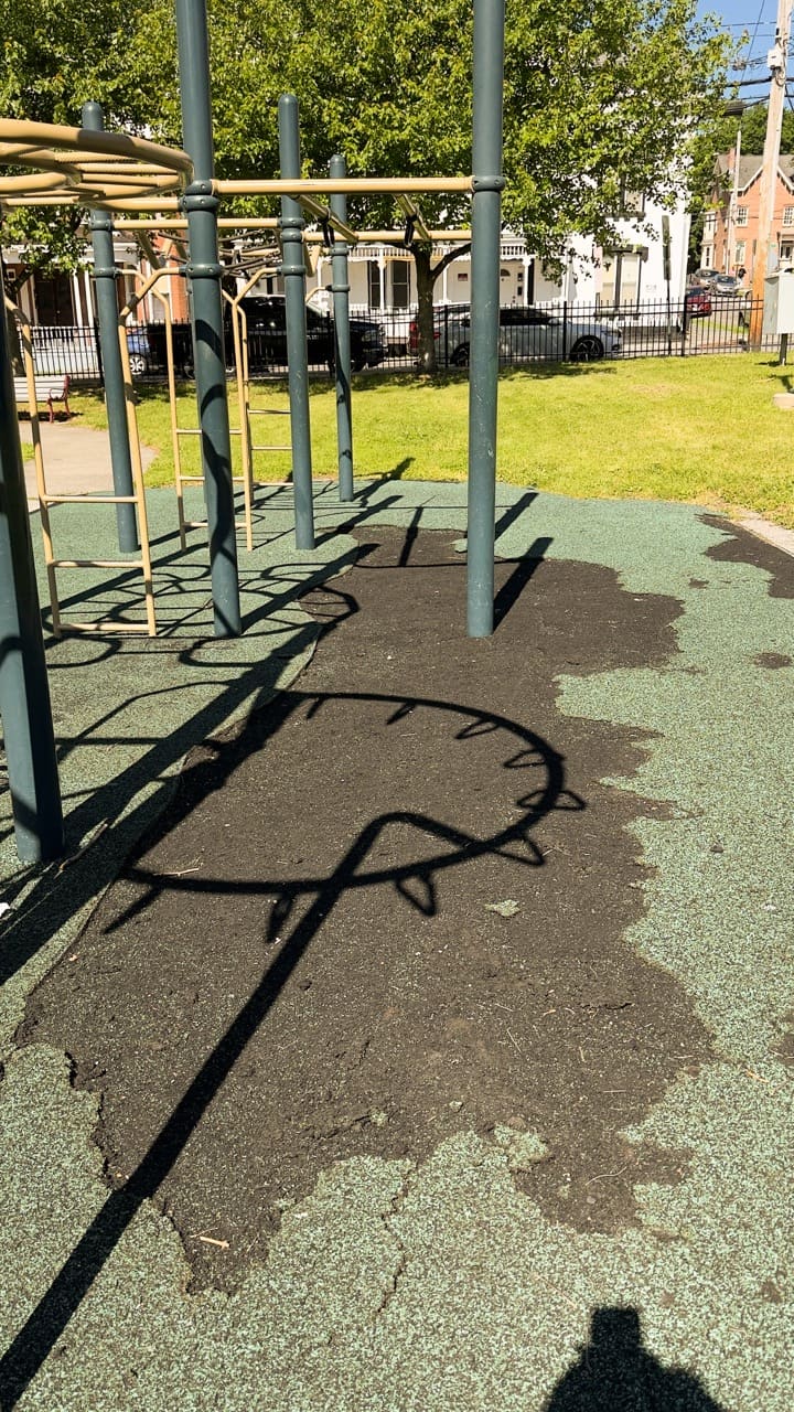A patch of black playground rubber pulled apart and exposed under climbing posts.