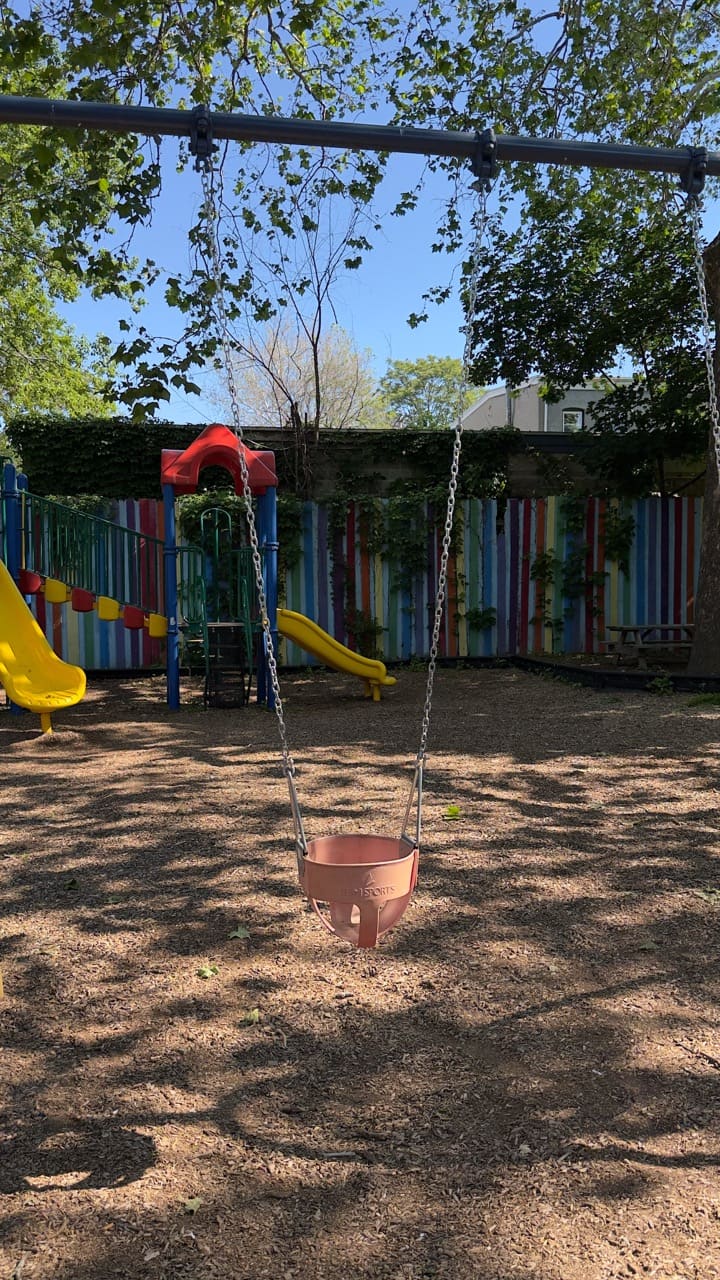 A worn black bucket-style baby swing hanging from chains.