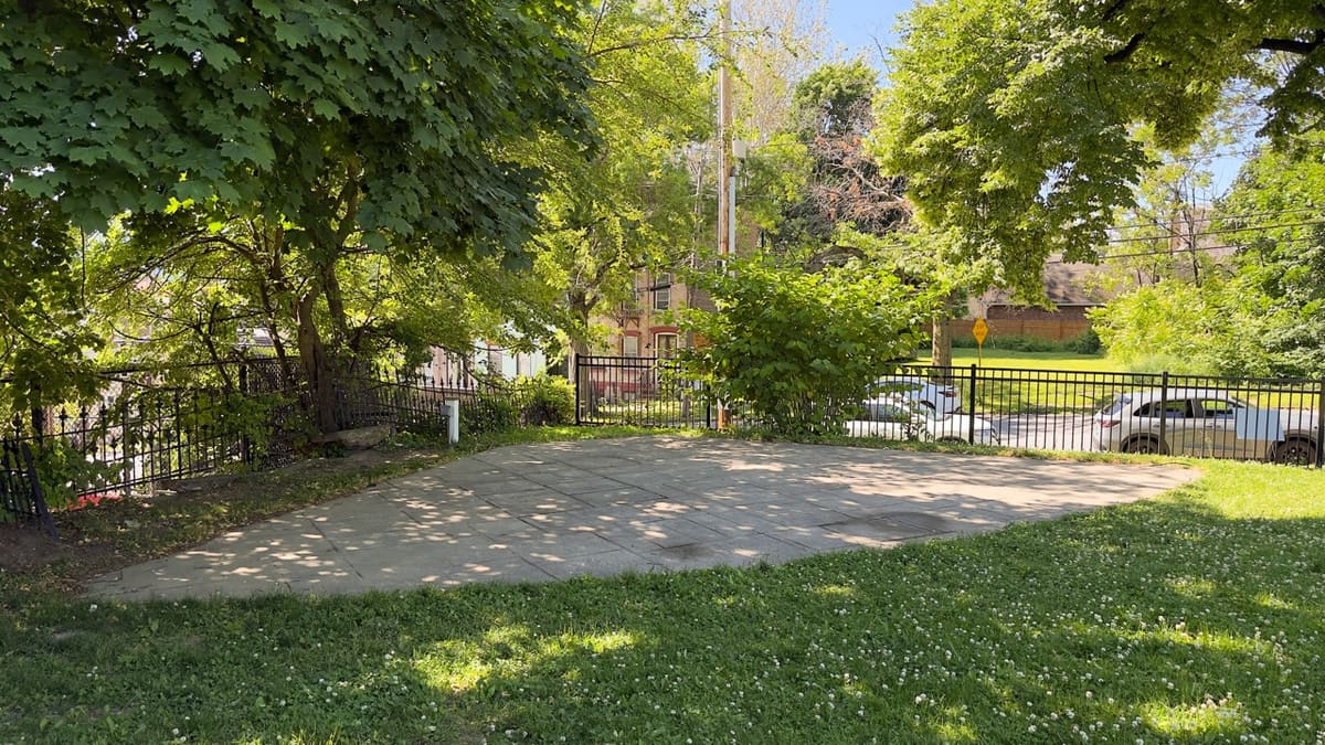 A small concrete pad inside Tyrone Crabb Park ringed by trees and an iron fence.