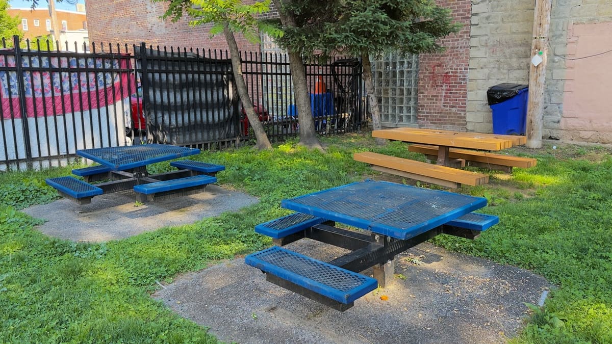 Two blue metal mesh picnic tables on cracked concrete pads.